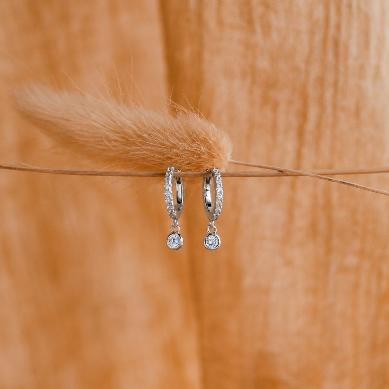 Pair of silver hoop earrings with clear stones on a wooden surface.
